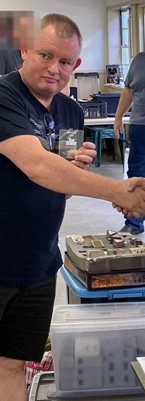 Adam Trapski shaking hands at a wargaming tournament, beside a box of miniature terrain